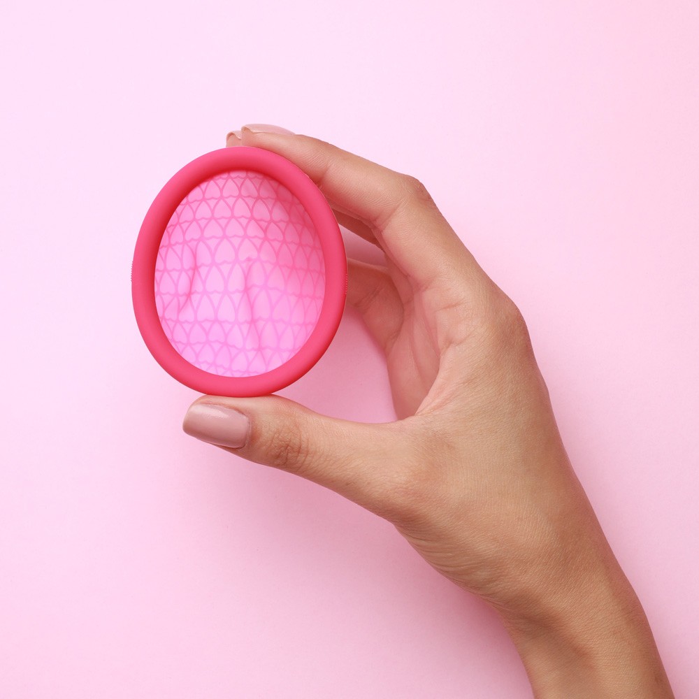 M�o segurando o Disco Menstrual Feminist de silicone m�dico cor-de-rosa, destacando sua flexibilidade e design.