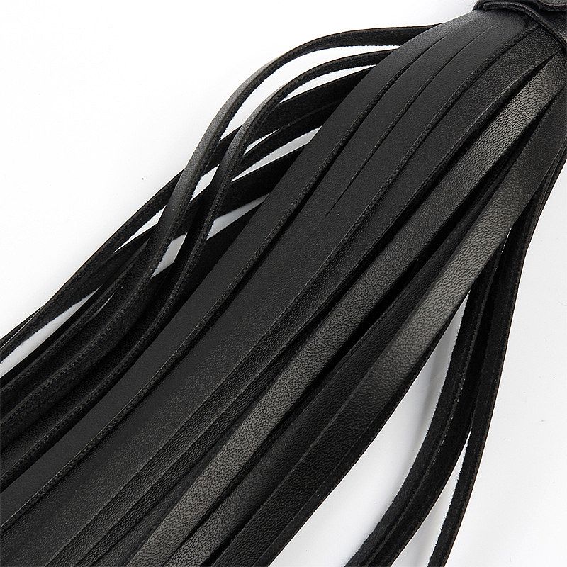 Close-up das tiras finas do flogger em PU preto, mostrando a textura do material