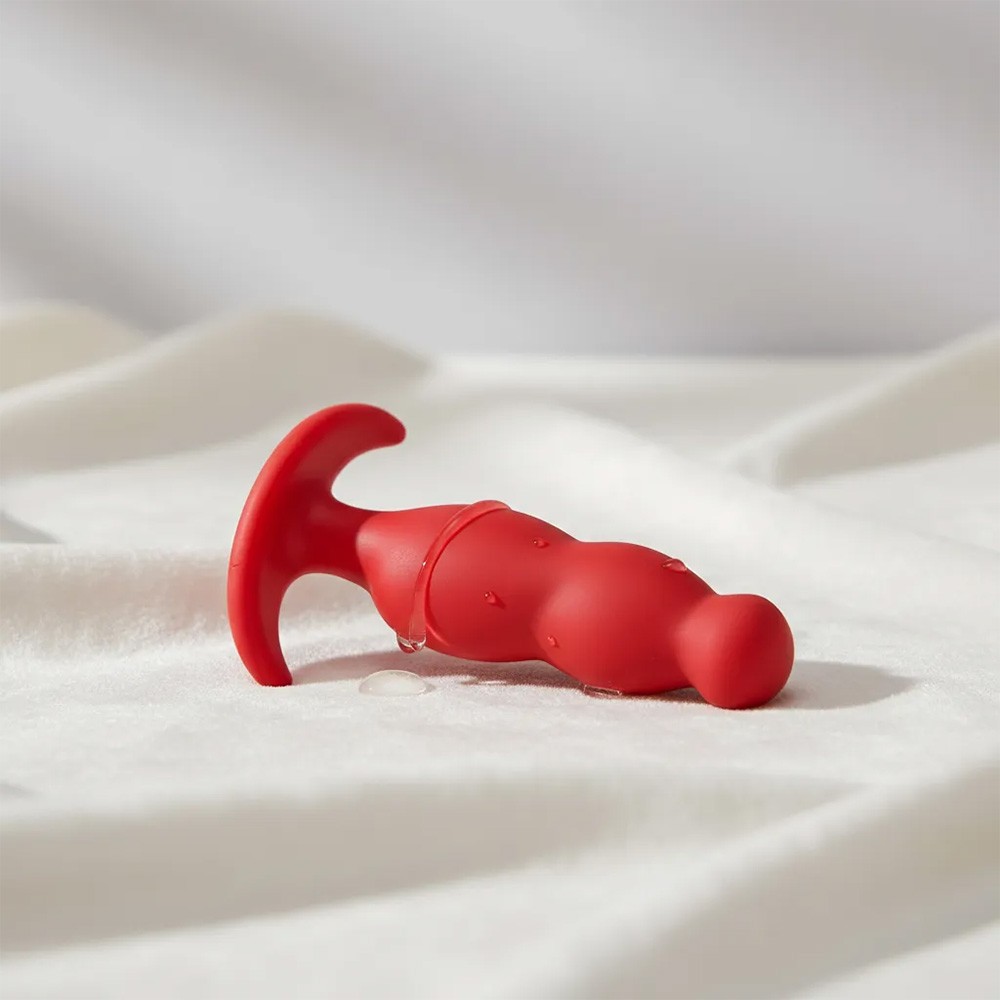 Plug Anal Mini Vermelho de silicone com corpo ondulado e base em T, com gotas de �gua em superf�cie branca