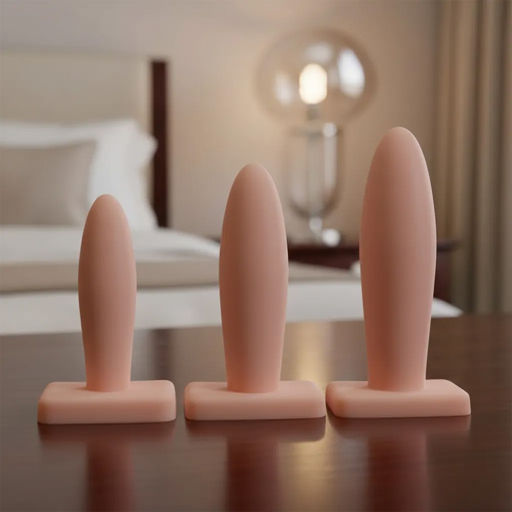 Kit Plug Anal B�sico de PVC Bege em ambiente de quarto, mostrando os tr�s tamanhos alinhados em uma superf�cie escura