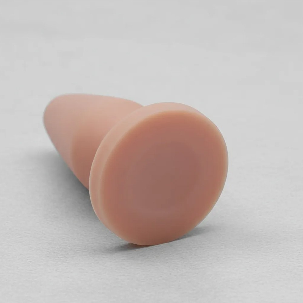 Detalhe da base de seguran�a arredondada do plug anal bege de PVC, em perspectiva de uso