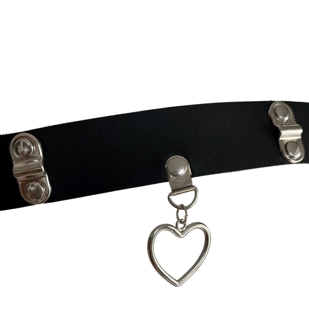 Vista frontal da coleira choker preta com pingente de cora��o em metal, mostrando a textura do PU e os bot�es de ajuste lateral