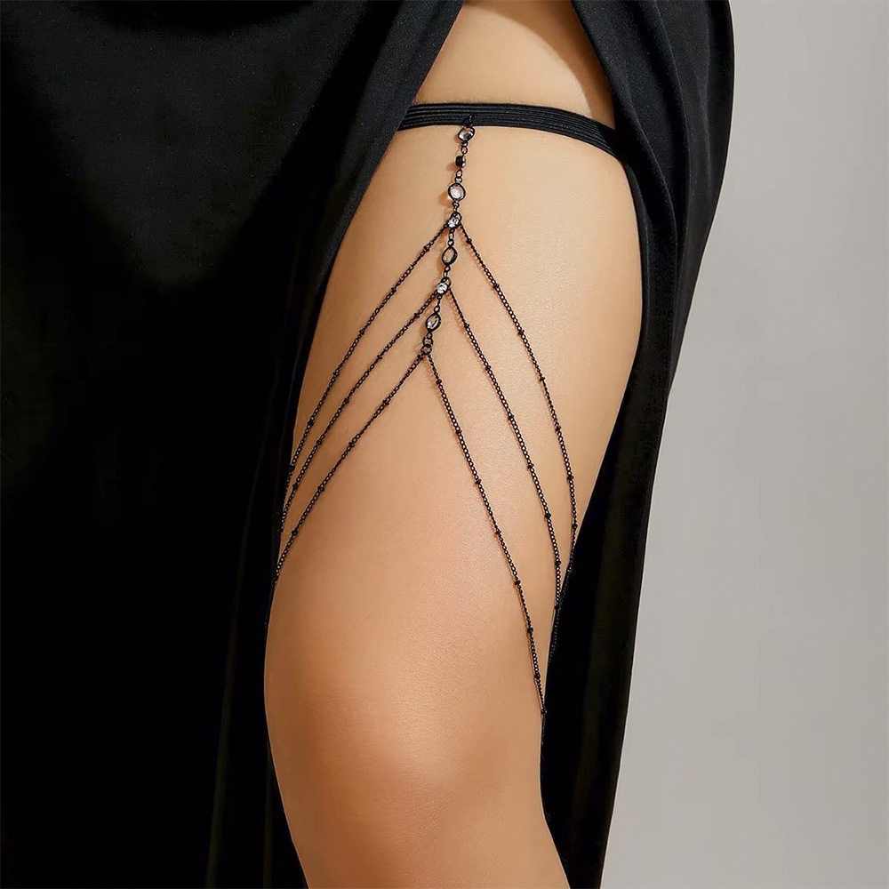 Joia de Corpo para Coxa com El�stico e Correntes com Detalhes em Strass Preta, em close na coxa, real�ando os detalhes em strass e o caimento das correntes.