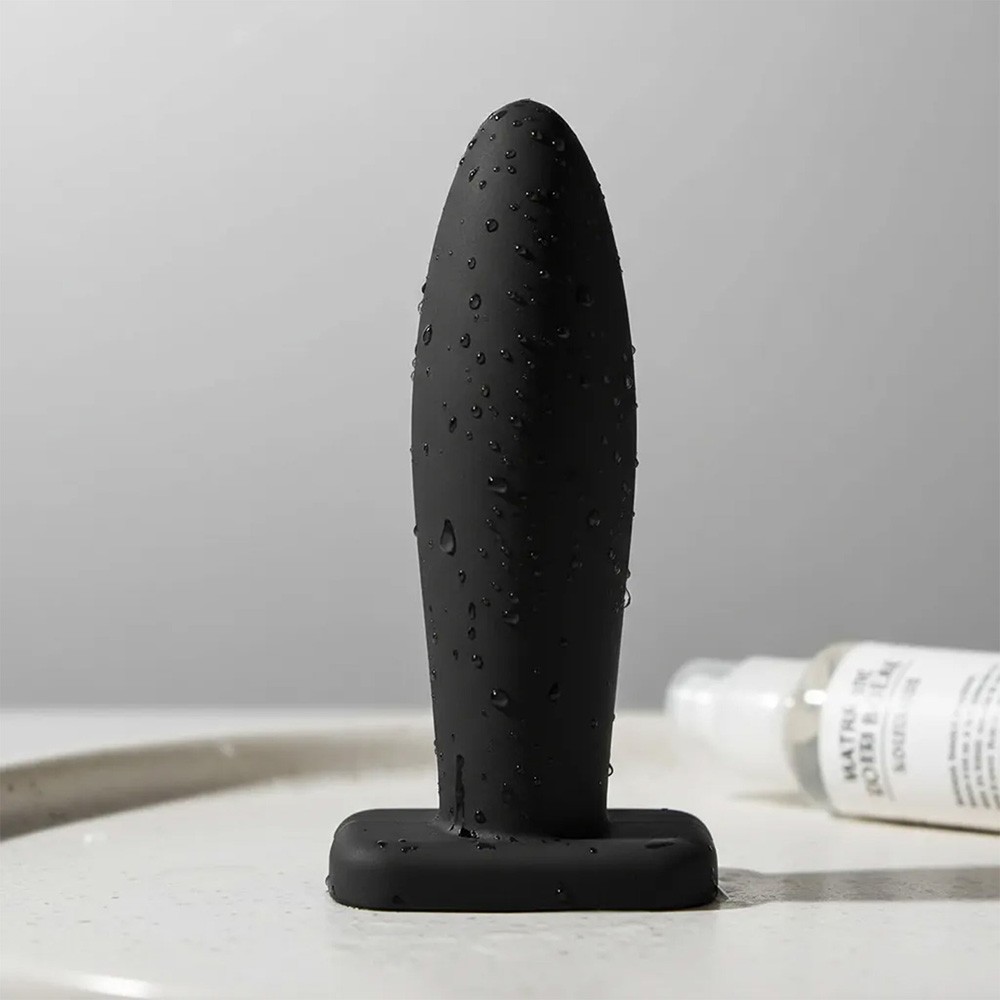 Plug anal preto em PVC flex�vel, molhado e com base de seguran�a em vista frontal, ao lado de um lubrificante