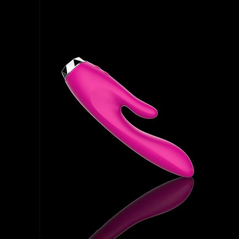 Vibrador Duplo Audrey Pink em silicone sobre fundo preto com reflexo, evidenciando o design e a cor vibrante