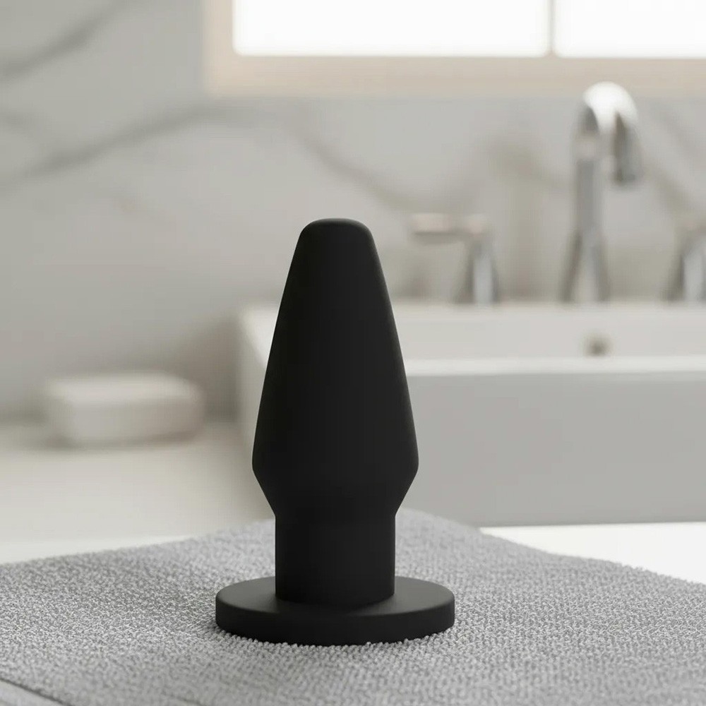 Plug anal de PVC flex�vel em um ambiente de banheiro, com toalha e pia ao fundo, destacando sua cor preta e design c�nico